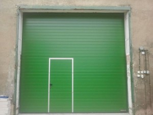 Priemyselná brána SPU40 s integrovanými dverami, vo farbe RAL 6002 listovo zelená.